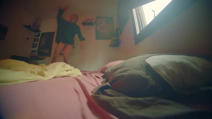 A young woman dances in a green shirt while standing on her bed