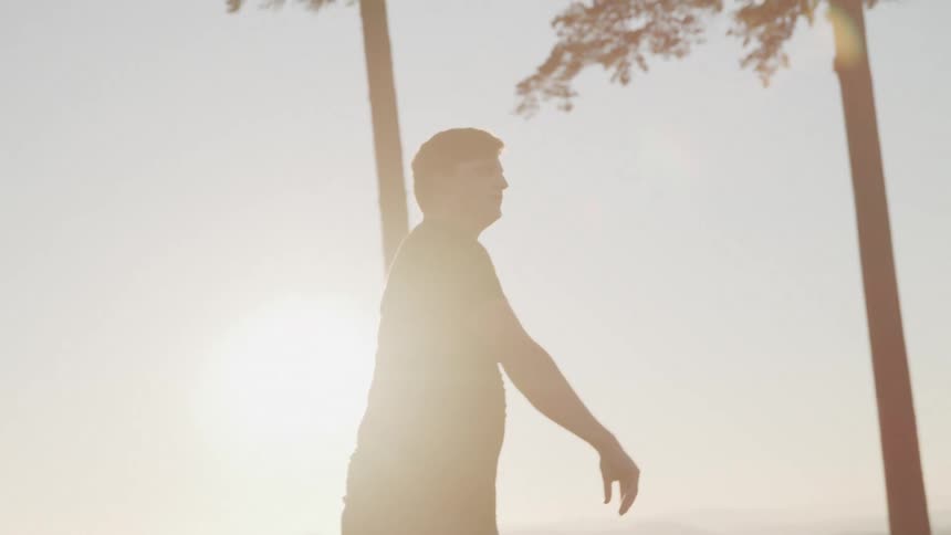 Man stretches outdoors with the bright sun in the background and plays baseball