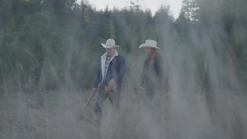 Male friends walk through a field near a grove of trees while out hunting