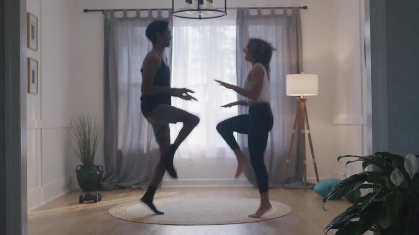 A couple performs high knee exercises together in their sunlit living room