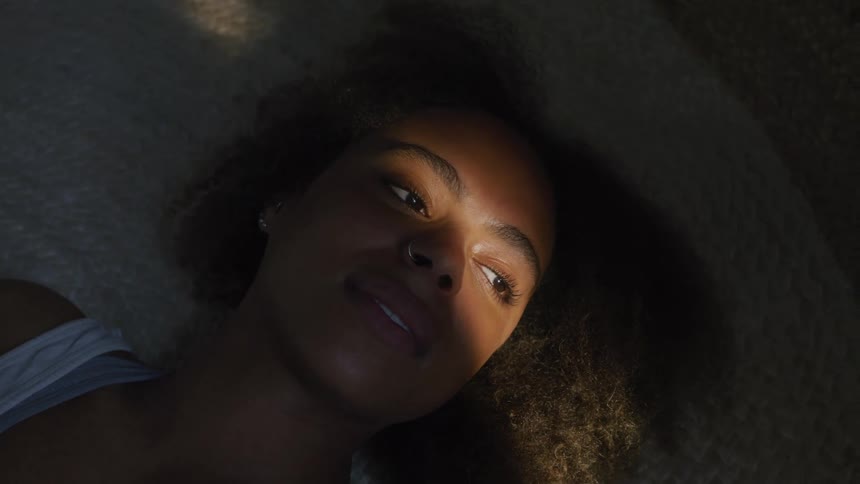 Sunlight shines onto the face of a woman lying on a bed and looking towards the window