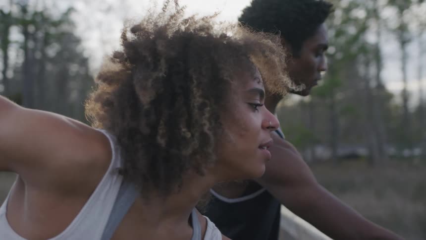 Man and woman stretch while on a footbridge near a grove of trees