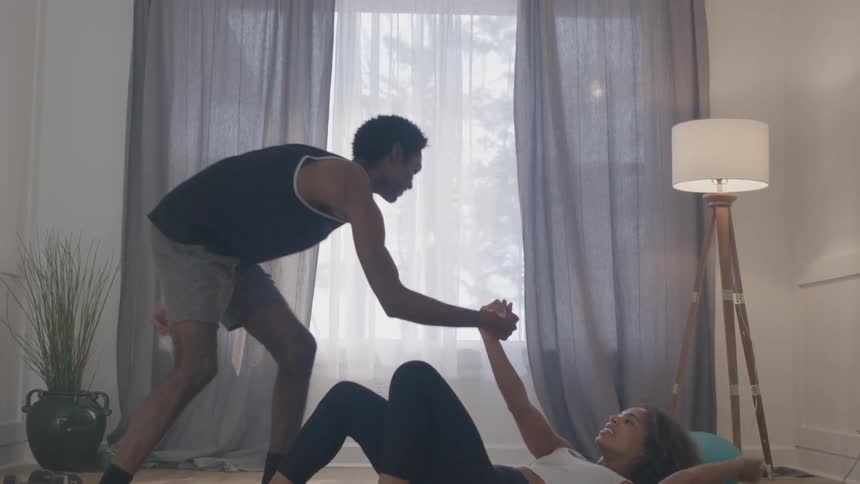Couple exercising at home while smiling and sharing a moment of mutual support