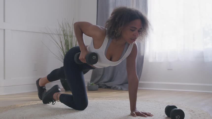 Woman balances on a knee while lifting a hand weight at home during the daytime