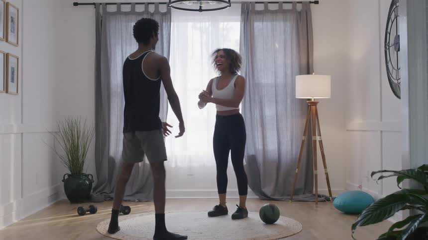 A man and woman are doing squats in their living room