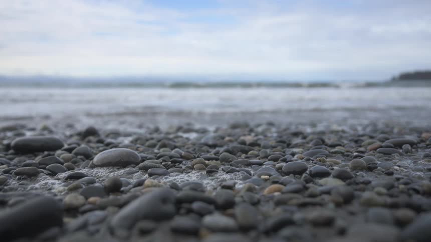 Many smooth and round pebbles on a beach with a small wave hitting them