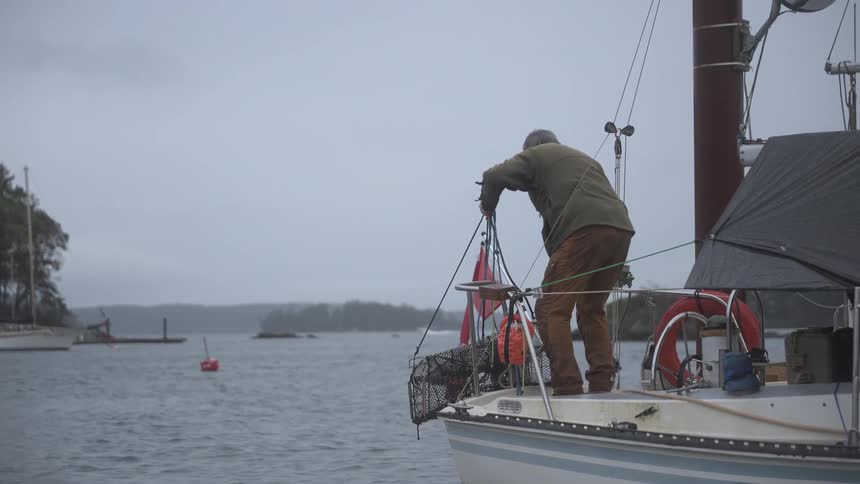 A man standing on a boat pulling a piece net that is on the edge and then he catches a crab that is inside it
