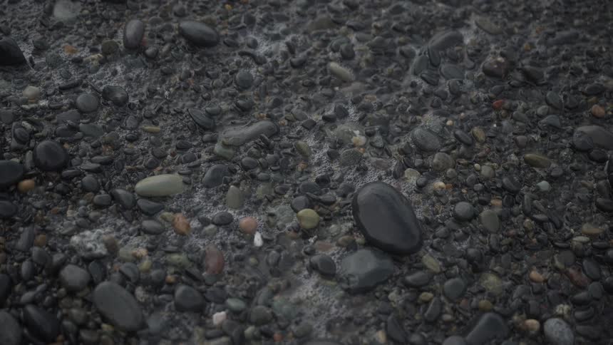Foam bubbles left by a wave on a pebble strewn beach slowly pop and disappear