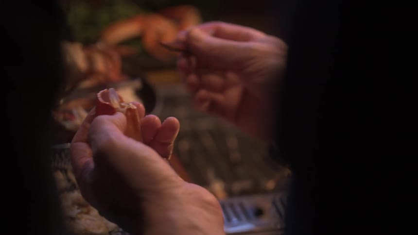 Two adults are removing the meat from crab claws near a stove burner