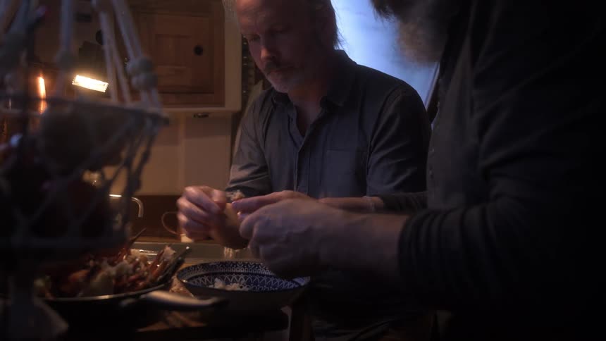 Two people prepare crab meat in a cramped dimly lit boat kitchen