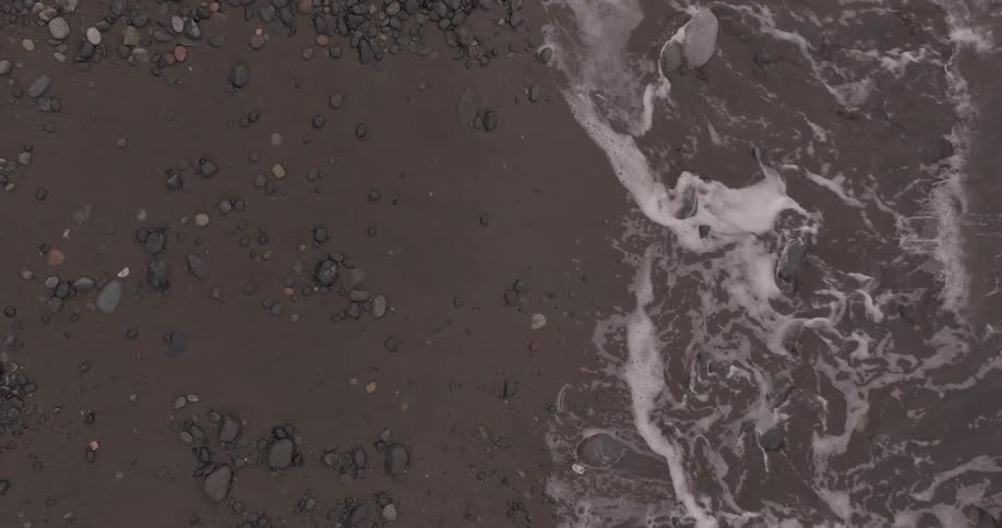 A rocky beach with dark sand and scattered stones where waves are gently washing ashore