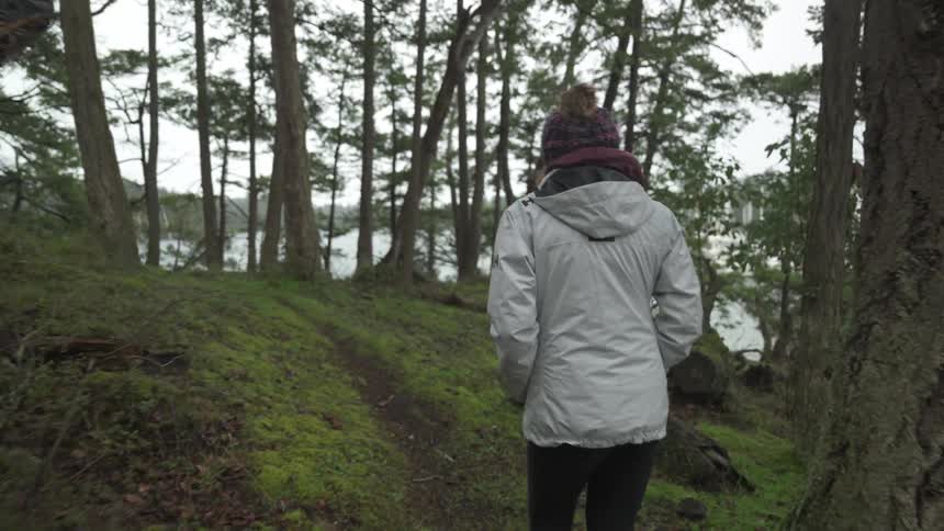 A woman in winter clothes and her hands in her pocket is walking on a path in the middle of a forest