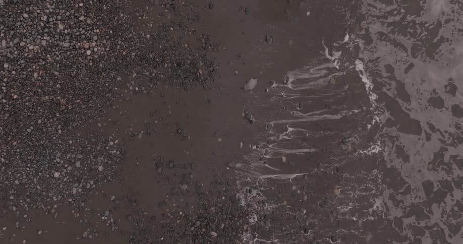 Birds eye view of tide gently rolling onto rocky shoreline