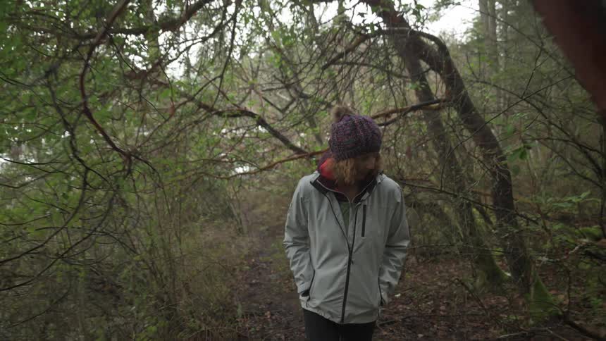 Woman wearing white jacket walking through grove of trees in the forest