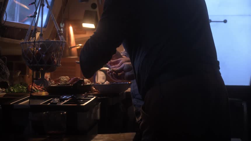 People tear crab meat apart over a pan on a stovetop in a cramped yet cozy kitchen setting