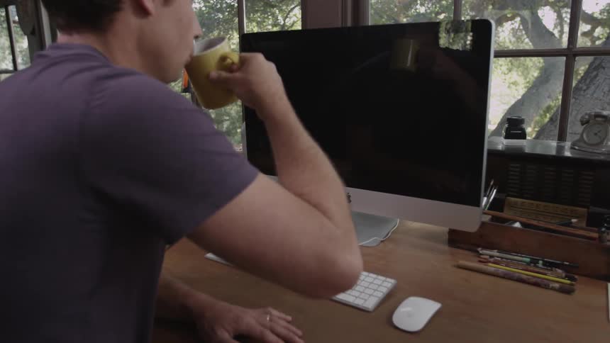 A man drinks coffee while sitting in front of a computer that isn't on