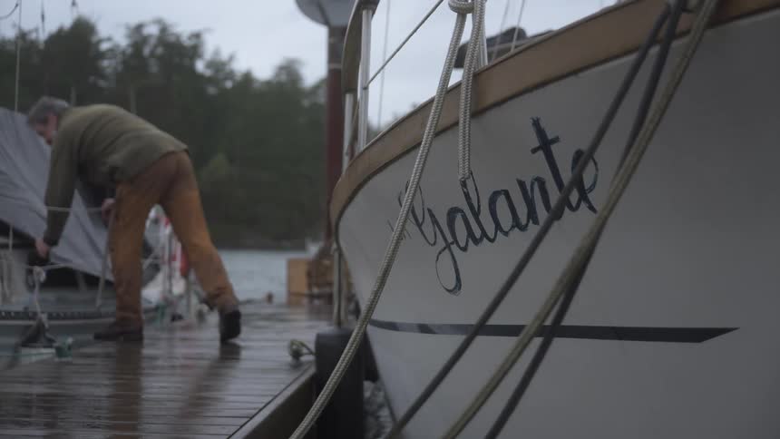 A person in a green shirt and tan pants works on a boat docked at a wet pier next to another boat named galante