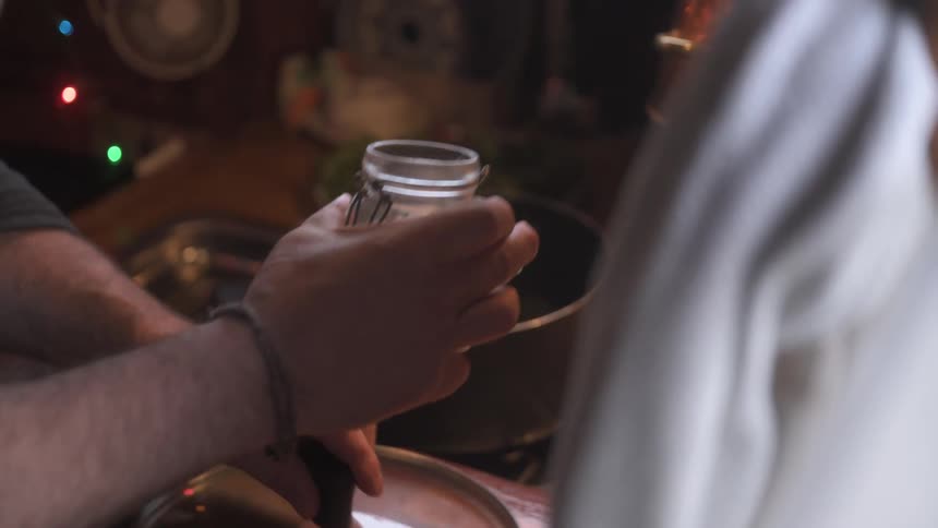 A person pours salt from a glass jar into a pot on a stovetop