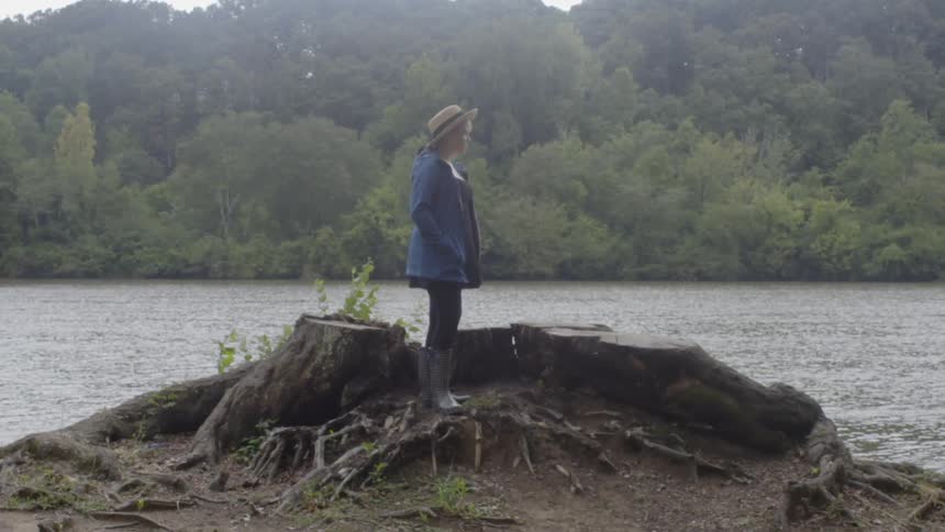 A woman is standing on an outlook made of tree trunks looking at a river