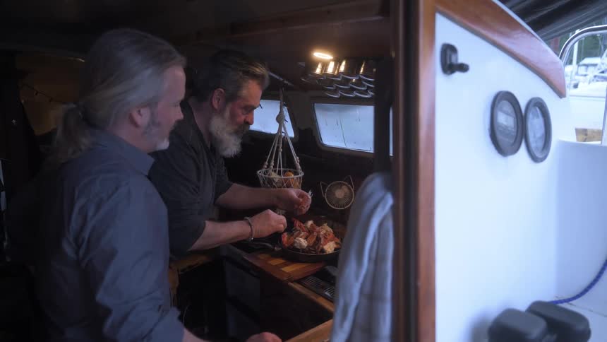 Man tasting a piece of crab next to another person in a cabin on a boat
