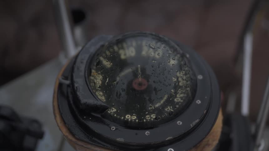 A closeup of a wet nautical compass with clear water droplets on its surface