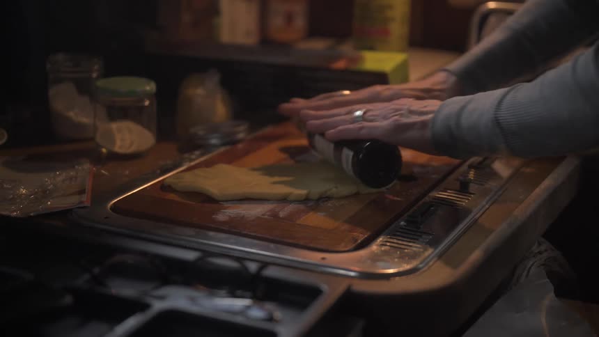 A person flattens dough using a bottle as a rolling pin on a board in a kitchen