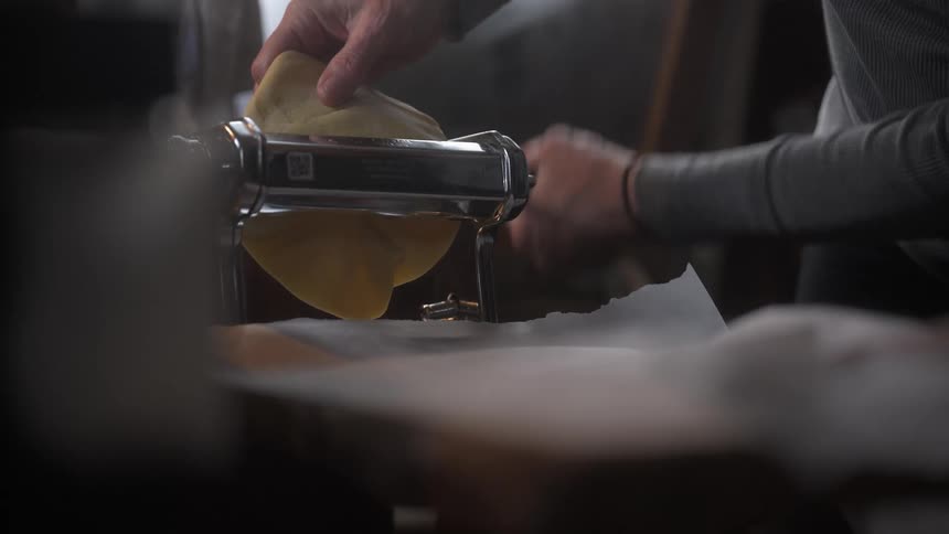 Pair of hands preparing bread dough by passing it through a metal instrument