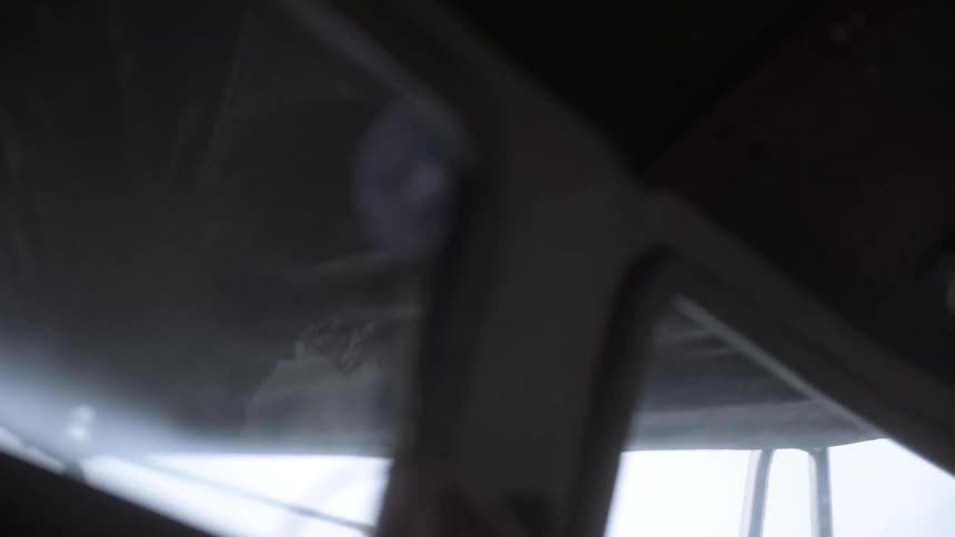 The reflection on a boat window reveals a person inside the cabin while outside a tarp flutters in the wind