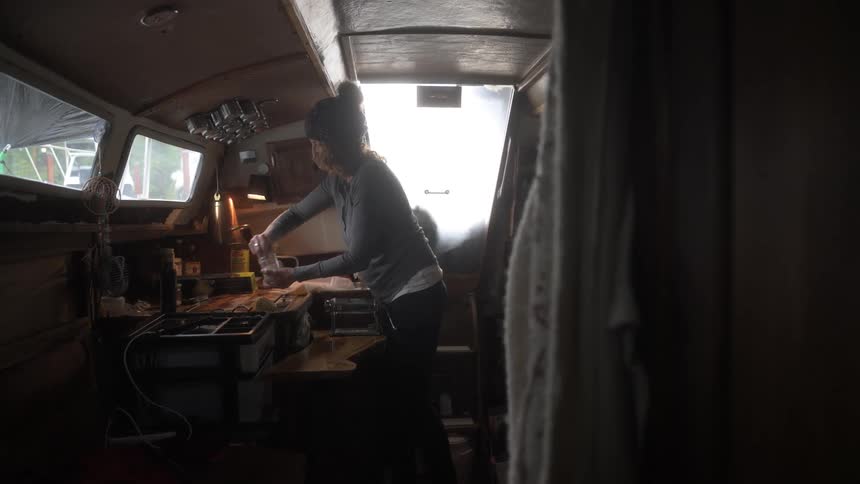 Woman sprinkles salt onto a surface while standing in the galley kitchen of a boat during the daytime