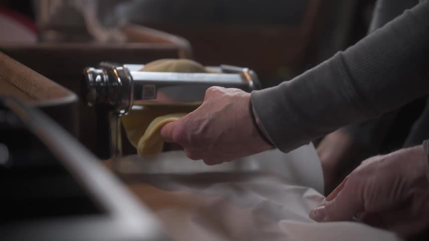 Two people are working with a dough that is being fed into a pasta machine