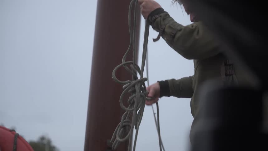 A man is on a pier on the water untangling a rope