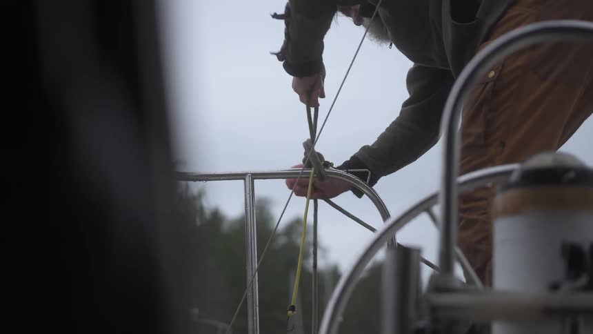 Man attaches a rope to the rail of a boat on an overcast day