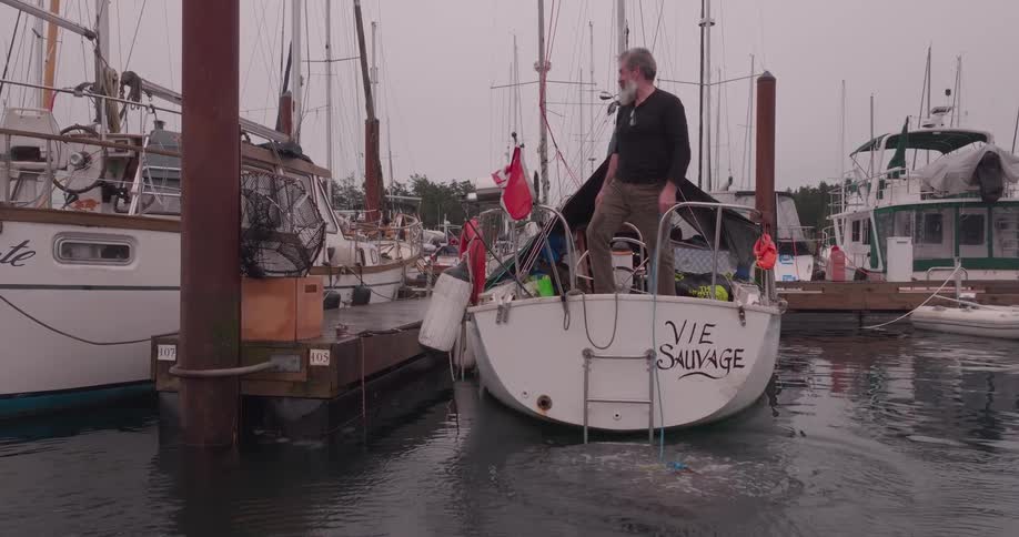 A man on a sailboat drops a homemade crab pot trap into the water