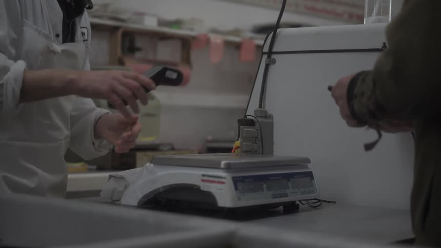 A customer in a deli puts his card in the machine after the worker sets it on the counter