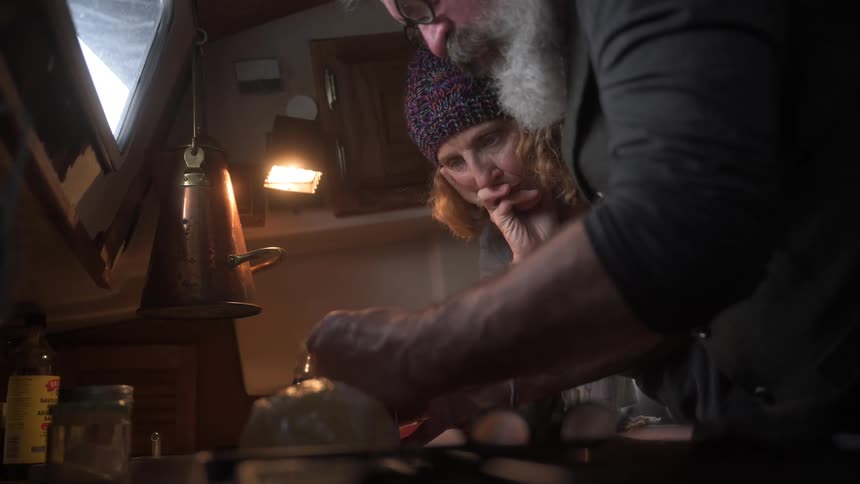 A man and woman lean over the stove top in the boat