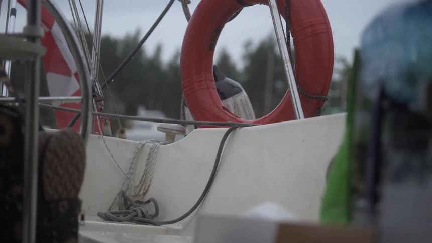 A close up view of a boat deck with a red life buoy ropes and equipment set against trees and a cloudy sky