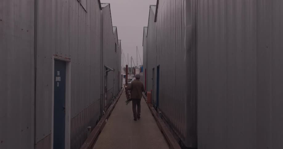 Person holding a fishing trap while walking towards a pier with boats