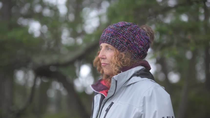 A woman is standing by the trees on a windy day