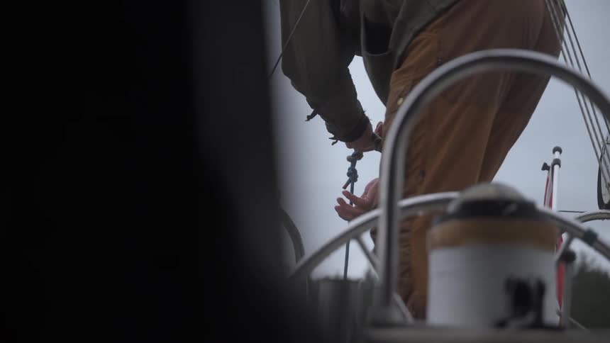 An adult lowers a rope while standing on a sailboat on a cloudy day