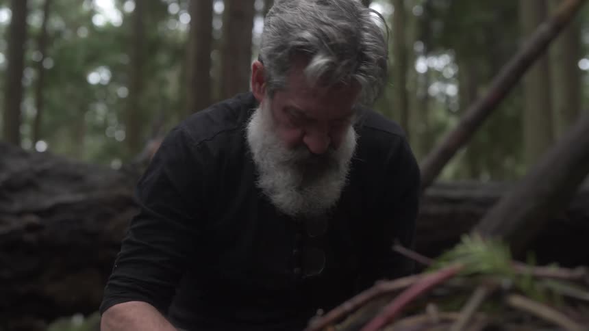 A man is starting a campfire in the woods