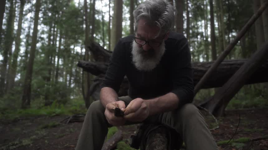 Man sitting in a forest handling a cutting knife