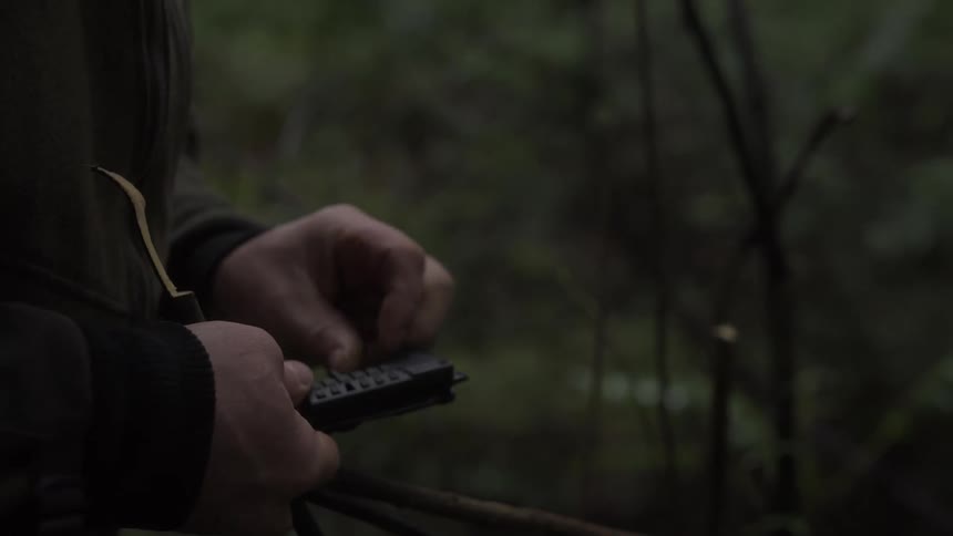 Man puts away a knife after using it in the woods to obtain a few slender sticks