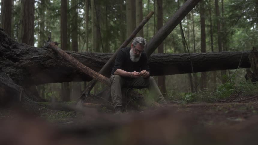 A footage of a man sitting beside a tree trunk in the woods
