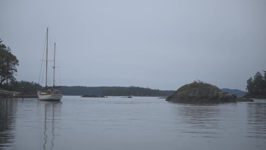 Small boat stopped in a calm sea with mountains in the background on a cloudy day