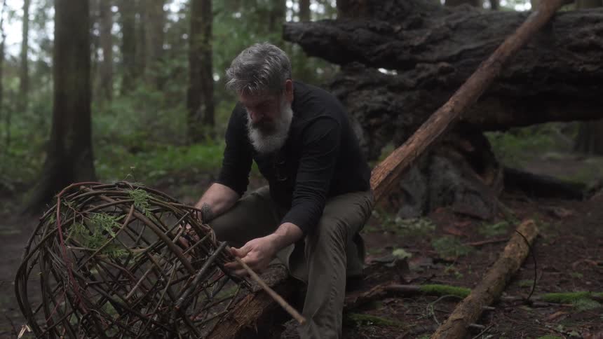 Man sitting in a forest setting a fishing trap with sticks