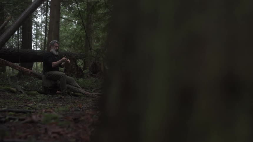 Man sitting in a forest making a wooden bow
