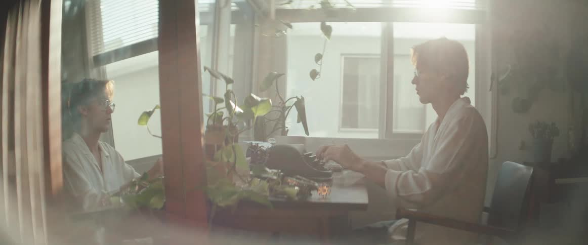 Man in a room putting on glasses and starting to type on an old typewriter
