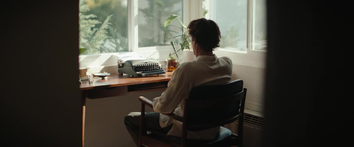 Man sitting in a chair facing a desk putting on glasses
