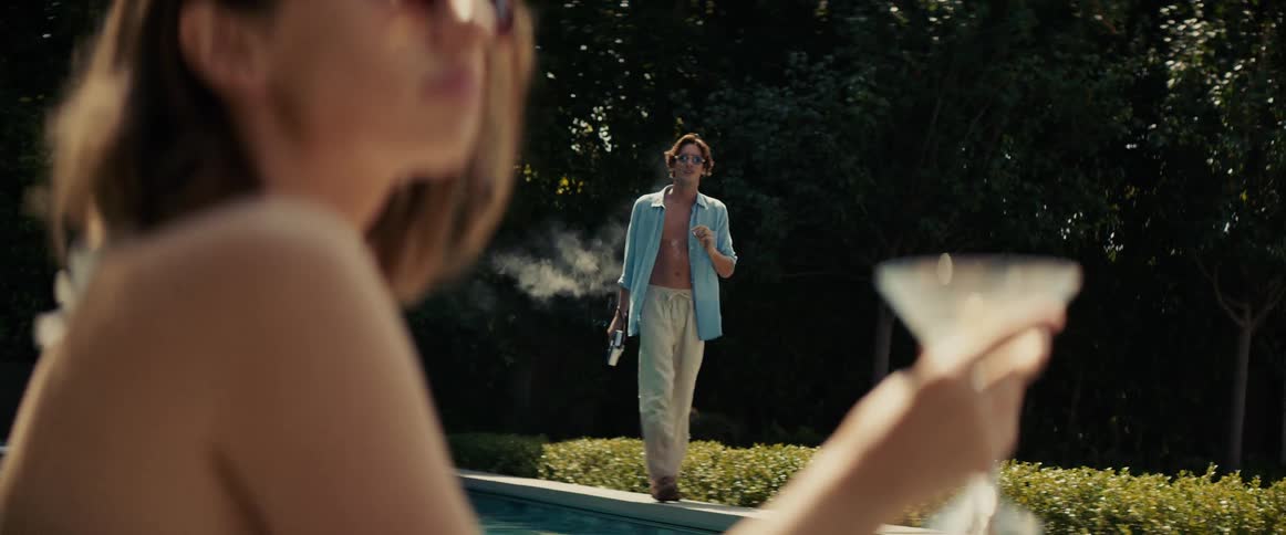 Woman in the foreground holding a drink and a man in the background smoking