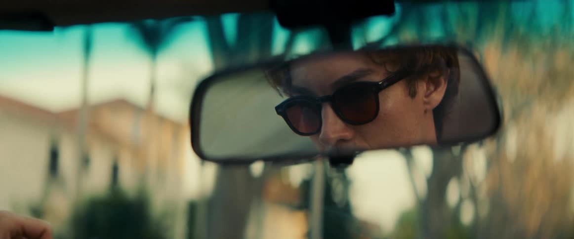 Face of a man wearing sunglasses seen through the rearview mirror of a moving vehicle